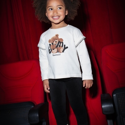 Camisola branca com urso estampado, leggings pretas e ténis pretos em cadeiras vermelhas