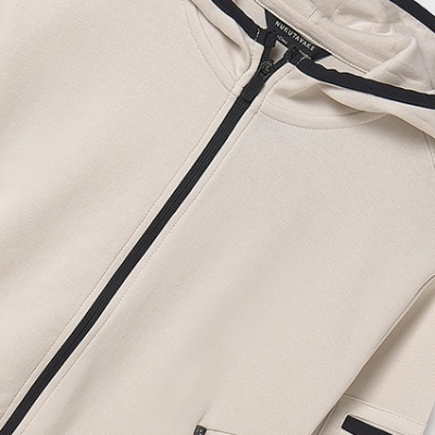 Casaco bege claro com capuz e fechos a preto, texto na manga