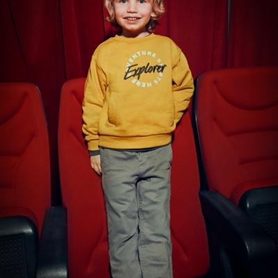 Menino com sweatshirt amarela e calças cinza numa cadeira vermelha de cinema