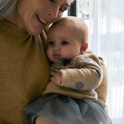 Mulher a segurar bebé vestido com camisola bege de bolinhas e saia de tule cinzenta