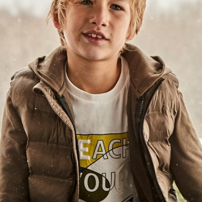 menino vestindo casaco castanho e t-shirt branca com texto em fundo desfocado