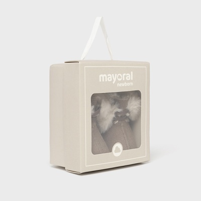 Embalagem bege com sapatinhos de bebé castanhos com pelo branco visíveis através de janela transparente.