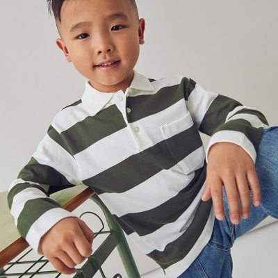 Menino a usar camisola de riscas verdes e brancas com gola polo e calças de ganga azuis