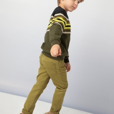 Criança de lado com camisola de riscas e calças verdes, sapatilhas castanhas