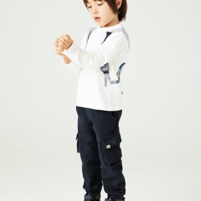 Criança vestida com t-shirt branca, calças pretas e ténis pretos sobre caixa de madeira