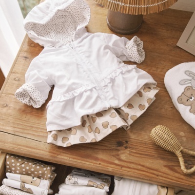 Conjunto de roupa de bebé branco e bege com padrões de bolinhas e maçãs em cima e dentro de uma gaveta de madeira