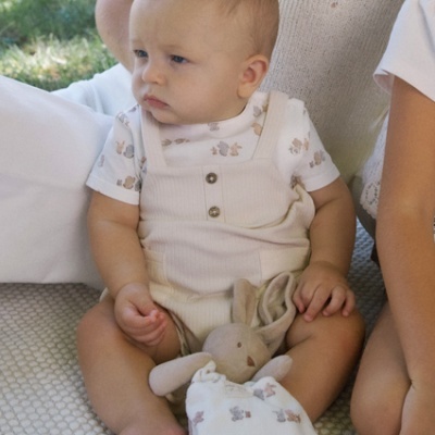 Bebé com roupa bege e branco sentado segurando peluche de coelho