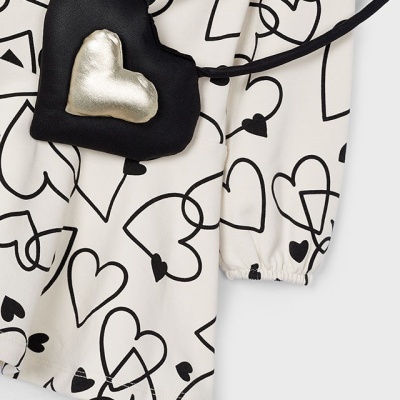 Peça de roupa branca estampada com corações pretos e bolsa preta em forma de coração com detalhe prateado.