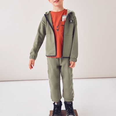 Menino com conjunto verde e t-shirt laranja em pé sobre livros