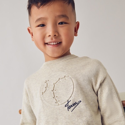 Camisola bege com bordado de bola de basebol e palavra Team usada por criança
