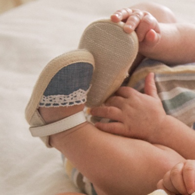 Sapatos para bebé azuis com renda branca e fecho branco, usados por bebé de roupa às riscas numa cama