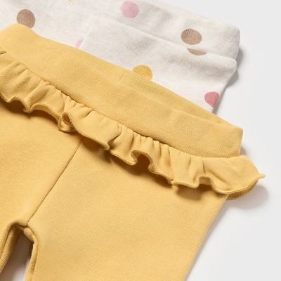 Calças amarelas com folhos para criança sobre tecido branco com bolinhas coloridas