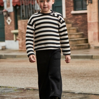 Criança com camisola riscada preta e branca e calças pretas a caminhar em rua molhada