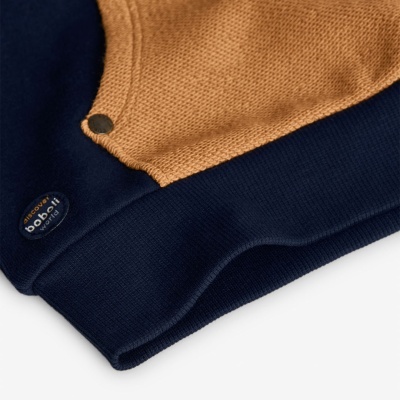 Peça de roupa de malha azul escuro e camel com botão metálico e etiqueta texturizada