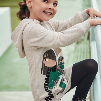 Criança com vestido bege estampado e leggings pretas, com sapatilhas pretas, segurando um corrimão verde