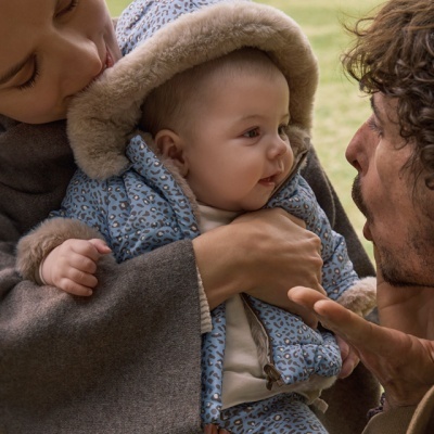 Casaco e calças de bebé azul com padrão e pelo bege, segurado por adultos no exterior