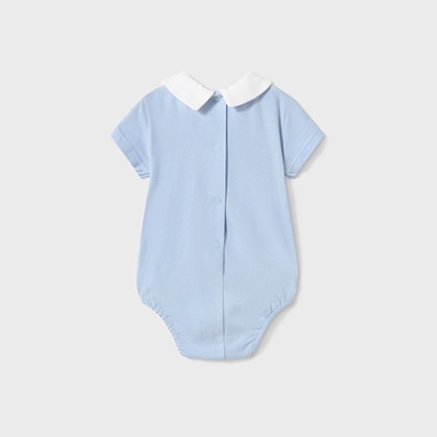 Body bebê azul celeste com gola branca e fecho de pressão numa superfície cinza claro