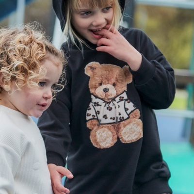 Duas crianças com roupa casual, vestido branco de malha e vestido preto com capuz e estampa de urso.