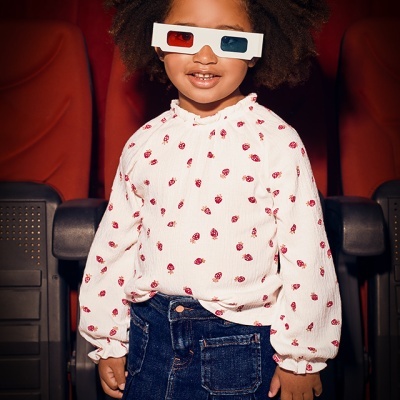 Criança com roupa branca com joaninhas e saia de ganga com óculos 3D em cinema