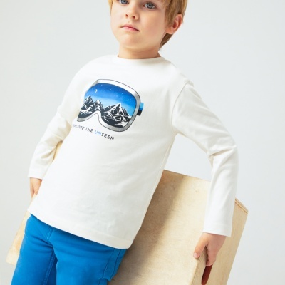 Menino com camisola branca estampada e calças azuis segurando caixa de madeira