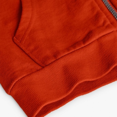 Detalhe de peça de roupa laranja com bolso e fecho éclair