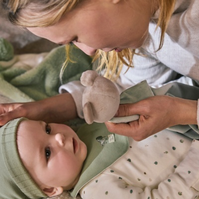 Bebé com roupa verde e branca a olhar para mulher que segura brinquedo de peluche