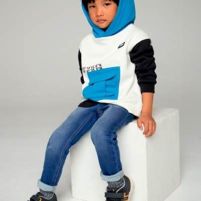 Criança sentada com roupa casual colorida sobre um cubo branco.