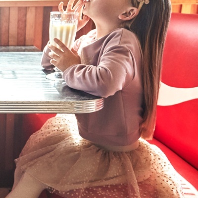 Menina em vestido rosa-bebé com saia de tule sentada num banco vermelho a beber de um copo alto