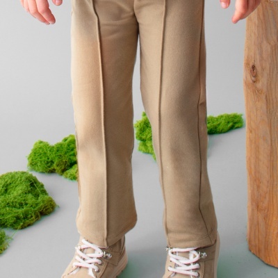 Calças de criança bege e botas bege claras com atacadores brancos num ambiente minimalista com musgo verde e tronco de madeira