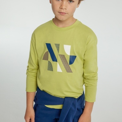 Menino com camisola verde de manga comprida com padrão geométrico e peça de roupa azul amarrada à cintura.