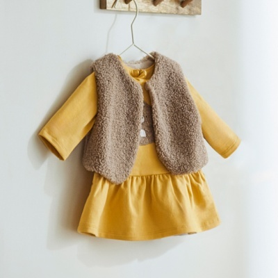 Veste de pelo castanha clara sobre vestido amarelo com manga comprida pendurada num cabide de metal