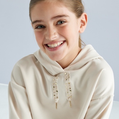 Menina com hoodie creme e cordões com tachas douradas