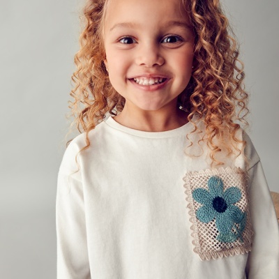 Menina a sorrir com jersey branco e bolso decorativo de tecido com flor azul
