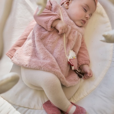 Bebé a dormir com roupa rosa e branca num berço acolchoado com brinquedo