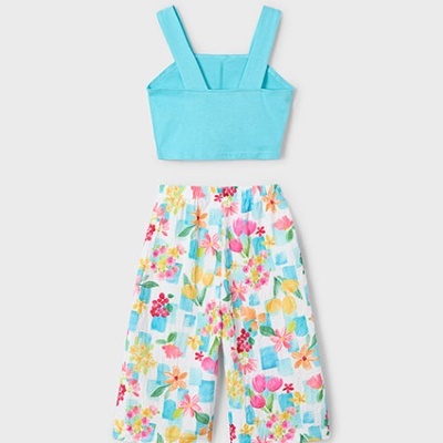 Conjunto de roupa azul turquesa e calças florais coloridas sobre fundo cinzento