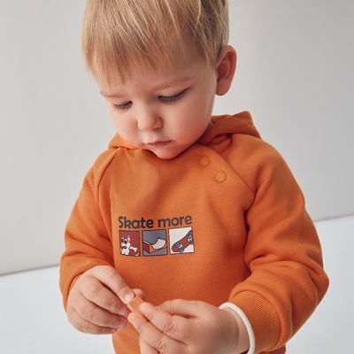 Criança com hoodie laranja estampado 'Skate more' em fundo claro