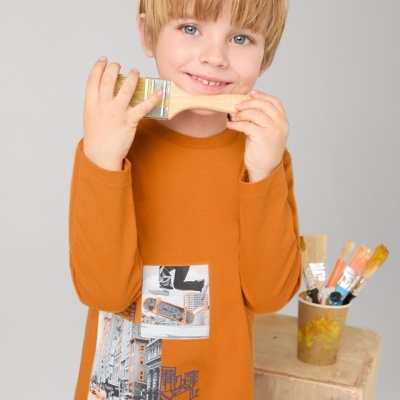 Camisola infantil laranja com estampado urbano e criança segurando pincel