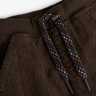 Detalhe de calças de cotelê castanho com cordão trançado multicolorido