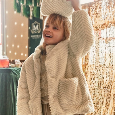 Criança com casaco peludo bege e mala pequena branca sobre a cabeça