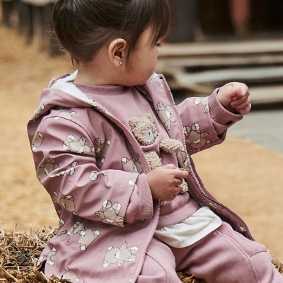 Criança com roupa rosa e casaco com padrão de ursos, sentada em pilha de feno ao ar livre.