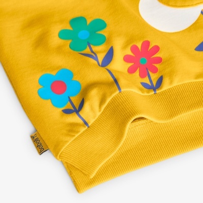 Detalhe de peça de roupa amarela com flores coloridas e punho canelado