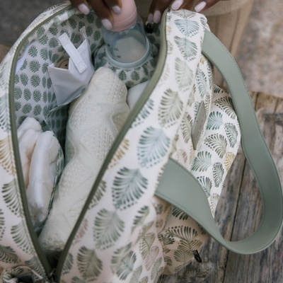 Saco de bebé com padrão de folhas verdes e interior forrado com o mesmo padrão, aberto com vários artigos para bebé.