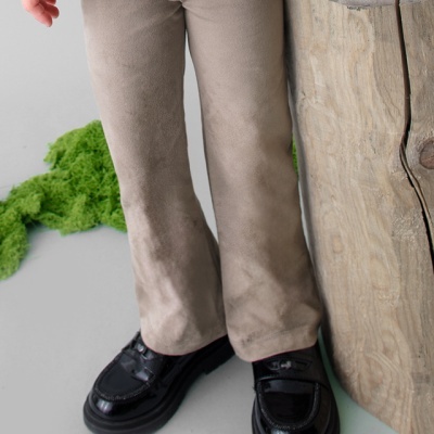 Criança vestindo calças castanho claro e sapatos pretos ao lado de um tronco de madeira