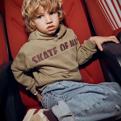 Criança com hoodie 'SKATE OF MI' sentada em cadeira vermelha de cinema