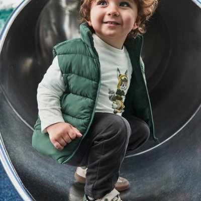 Menino com casaco verde e sapatilhas sentado num escorregador metálico