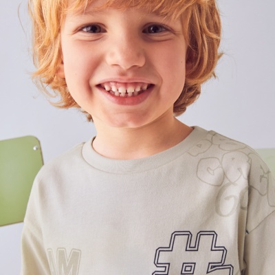 Camisola cinza claro com padrões de hashtags e letras, usada por criança ruiva