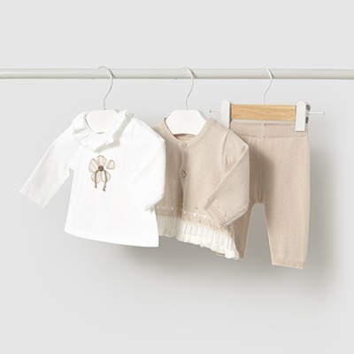 Conjunto de roupa de bebé branco e bege pendurado em cabides.