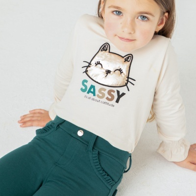 Menina com camisola branca estampada de gato e calças verdes