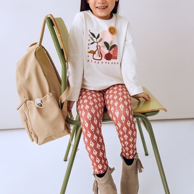 Menina sorridente sentada numa cadeira verde com roupa colorida e mochila bege