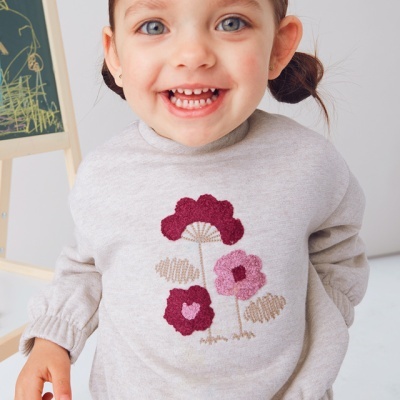 Camisola bege de criança com flores bordadas usada por menina sorridente